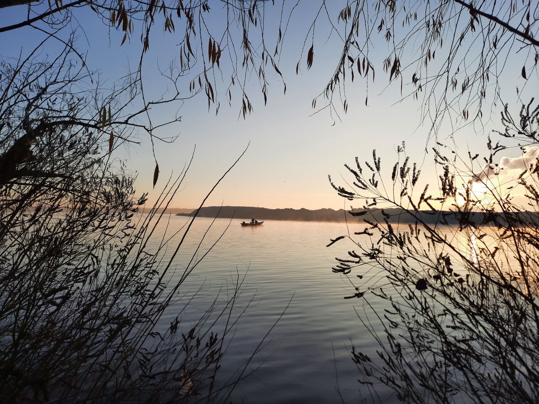 Peaceful fishing on a calm river at sunrise, with a boat in view.